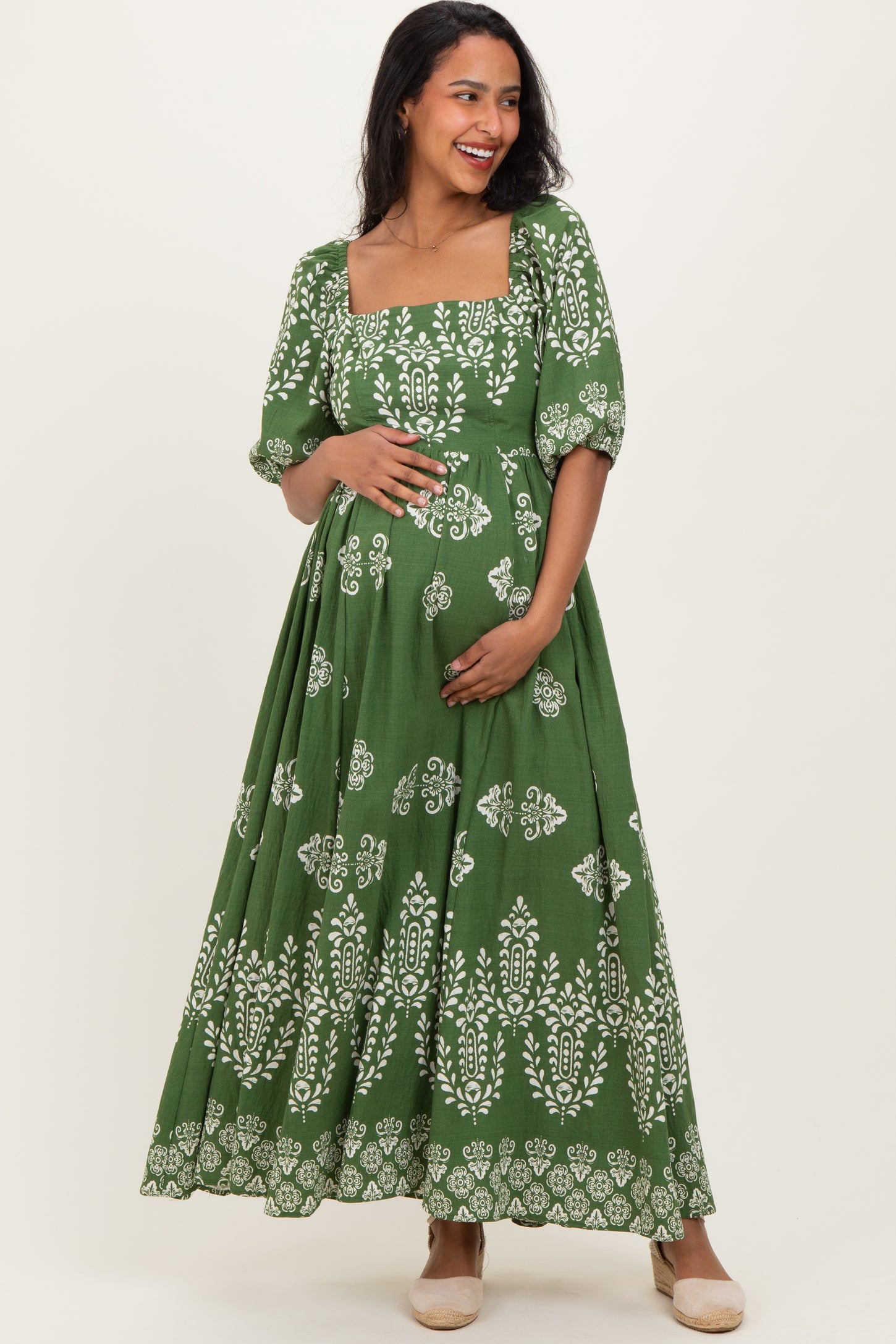 woman wearing a green maternity dress with white floral patterns and short puff sleeves, holding her baby bump