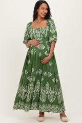 woman wearing a green maternity dress with white floral patterns and short puff sleeves, holding her baby bump