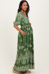 woman wearing a green maternity maxi dress with a white floral print and side pockets, showing her baby bump