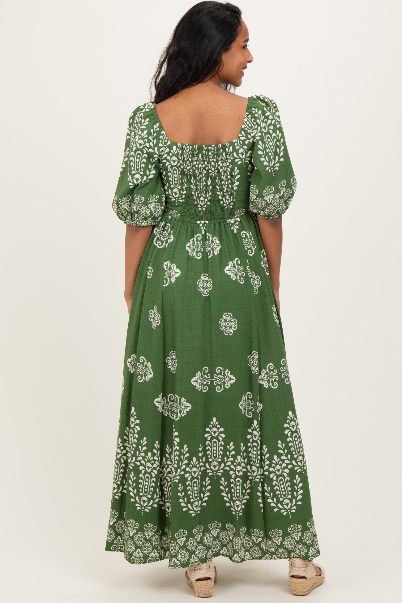 woman wearing a green floral print maternity maxi dress with puff sleeves and a smocked back design