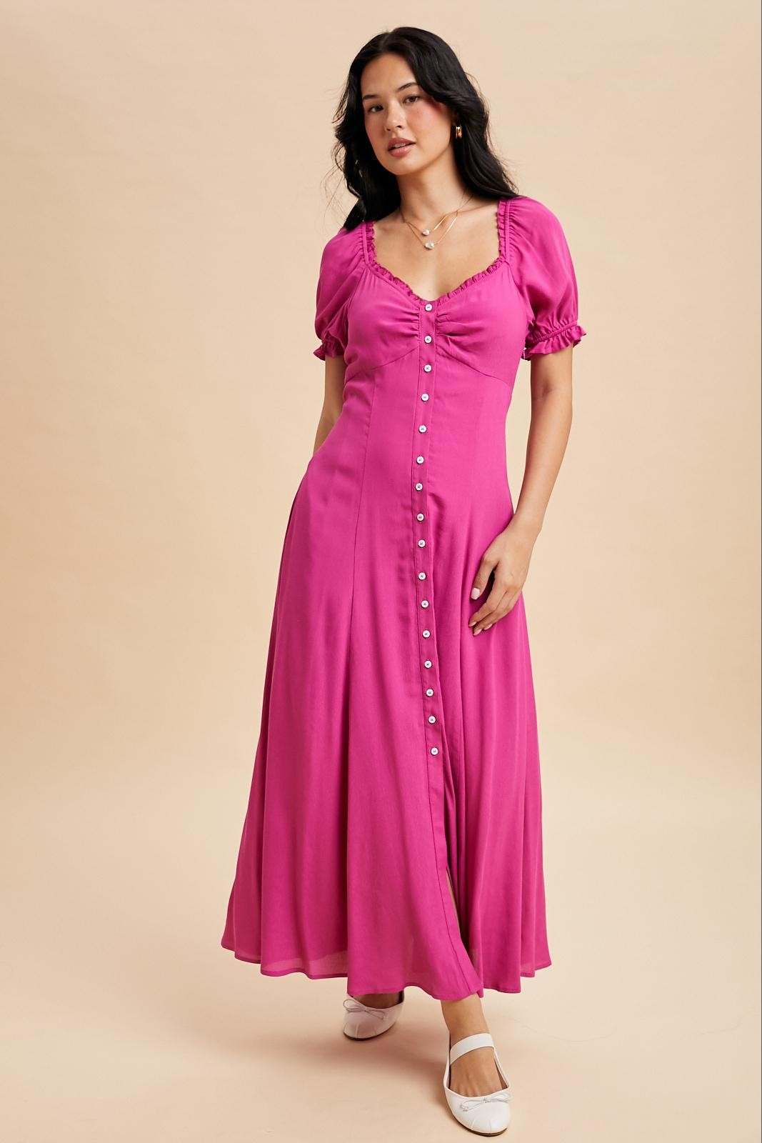 woman wearing a bright pink maxi dress with puff sleeves and button details, standing on a neutral background