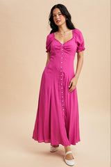 woman wearing a bright pink maxi dress with puff sleeves and button details, standing on a neutral background