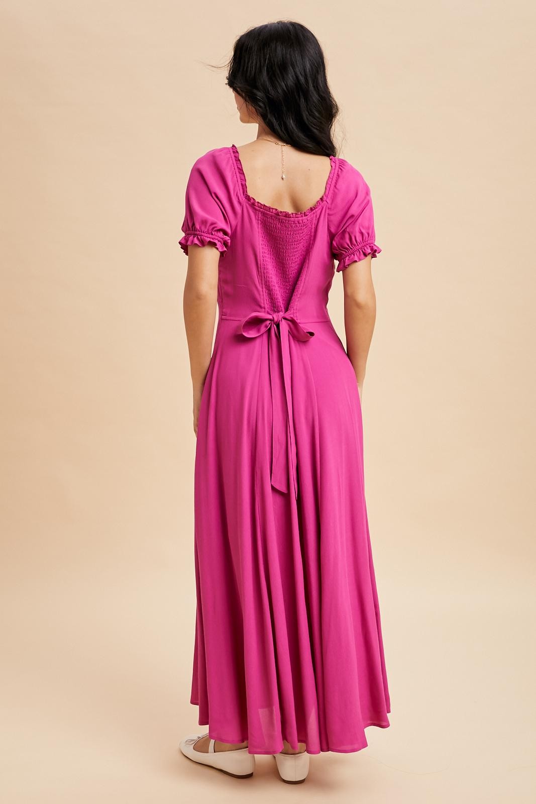 woman wearing a pink maxi dress with puff sleeves and a bow detail at the back