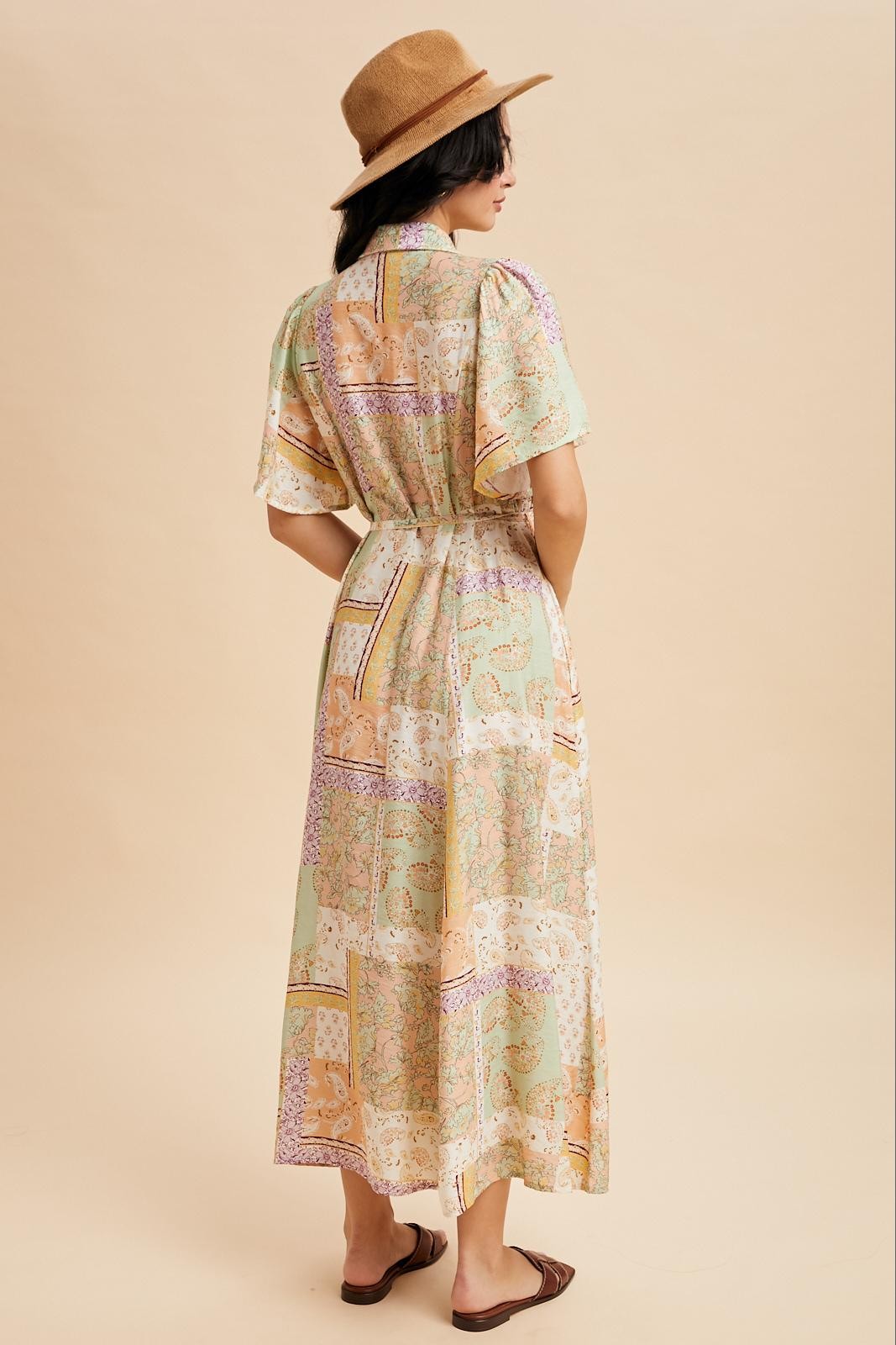 woman wearing a pastel patterned maxi dress with short sleeves and a cinched waist, styling a tan hat and sandals