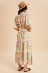 woman wearing a pastel patterned maxi dress with short sleeves and a cinched waist, styling a tan hat and sandals