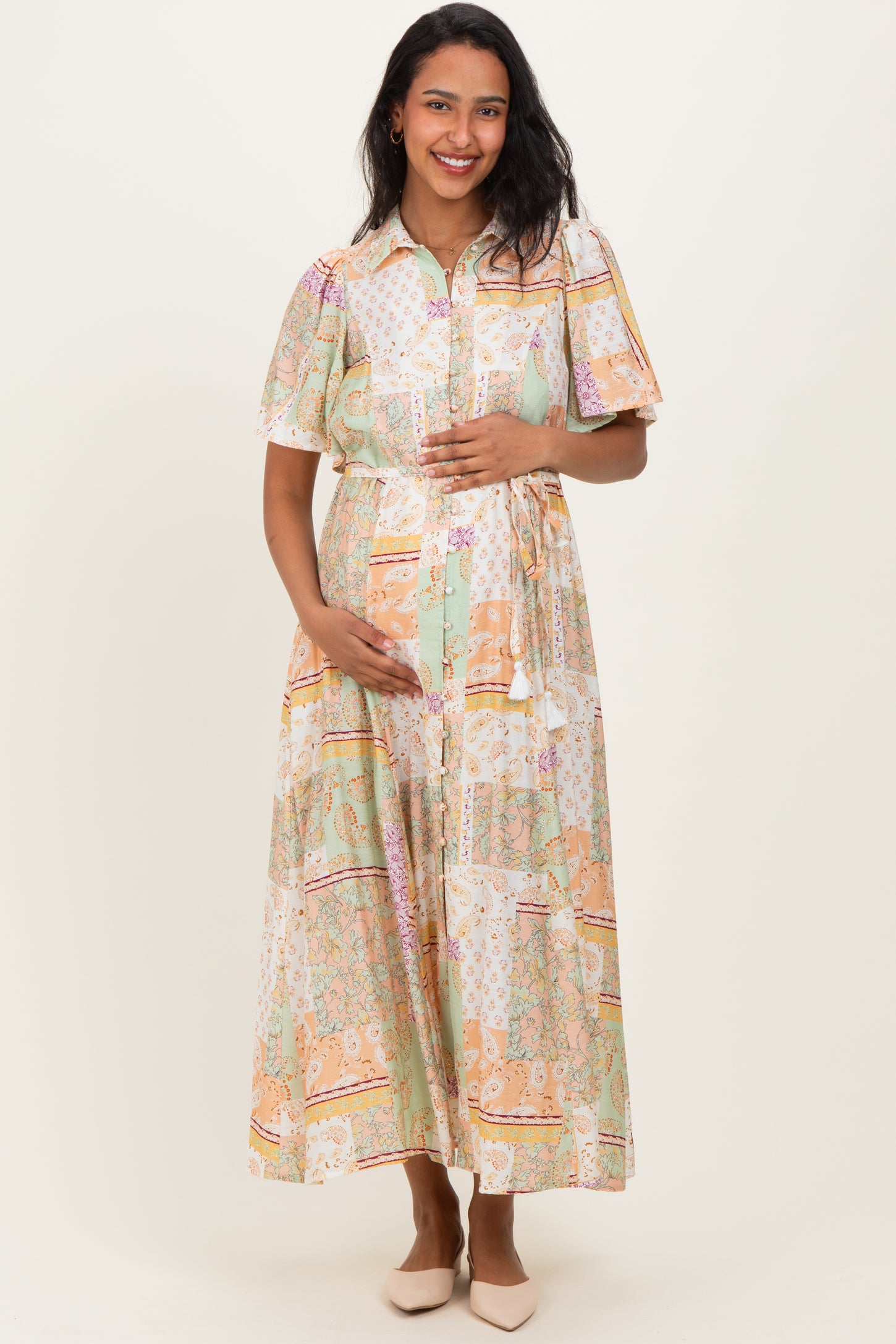 woman wearing a patterned maternity maxi dress with short sleeves and a tied waist, holding her baby bump