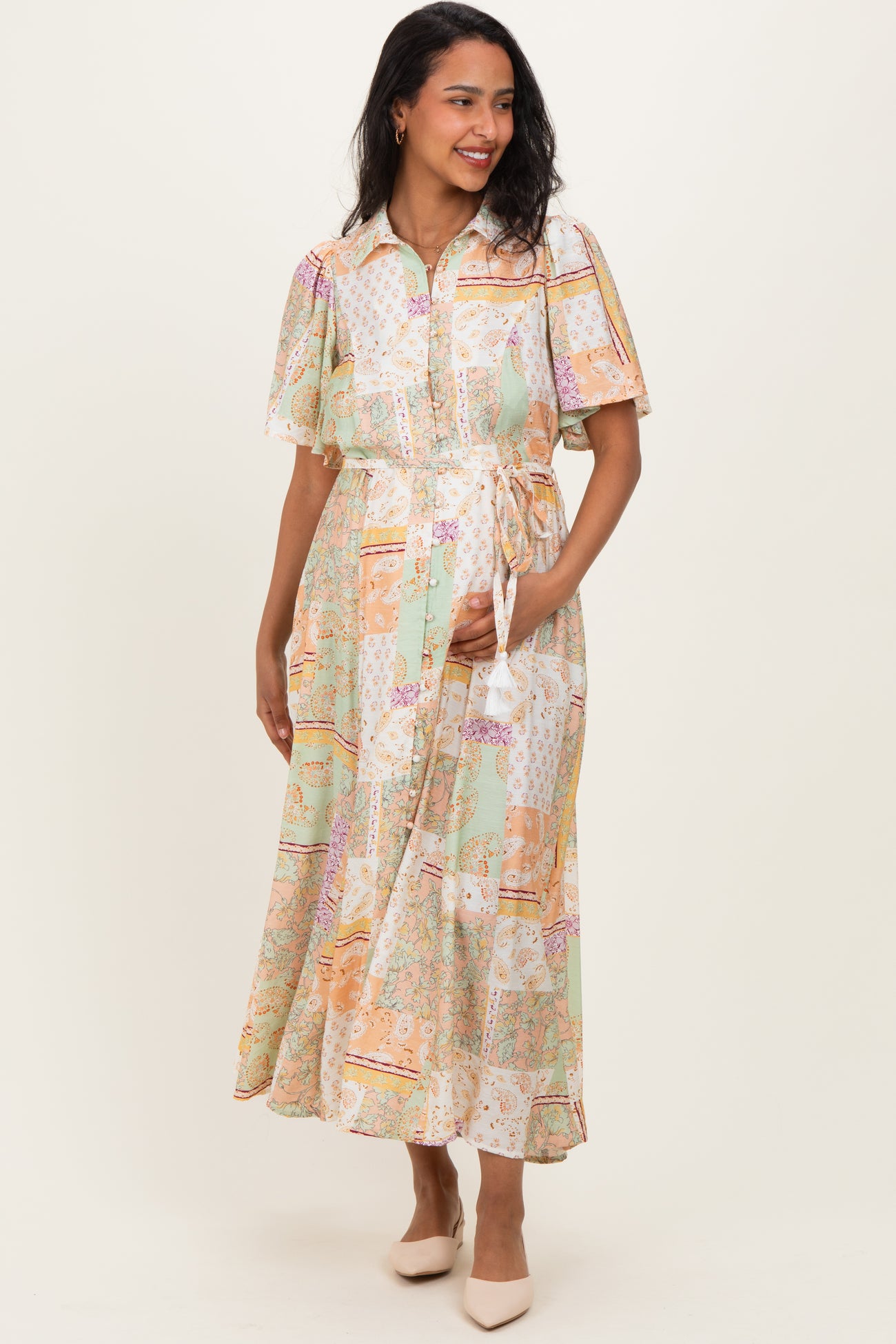 woman wearing a multi-colored floral maternity dress with short sleeves and a tie waist, holding her baby bump