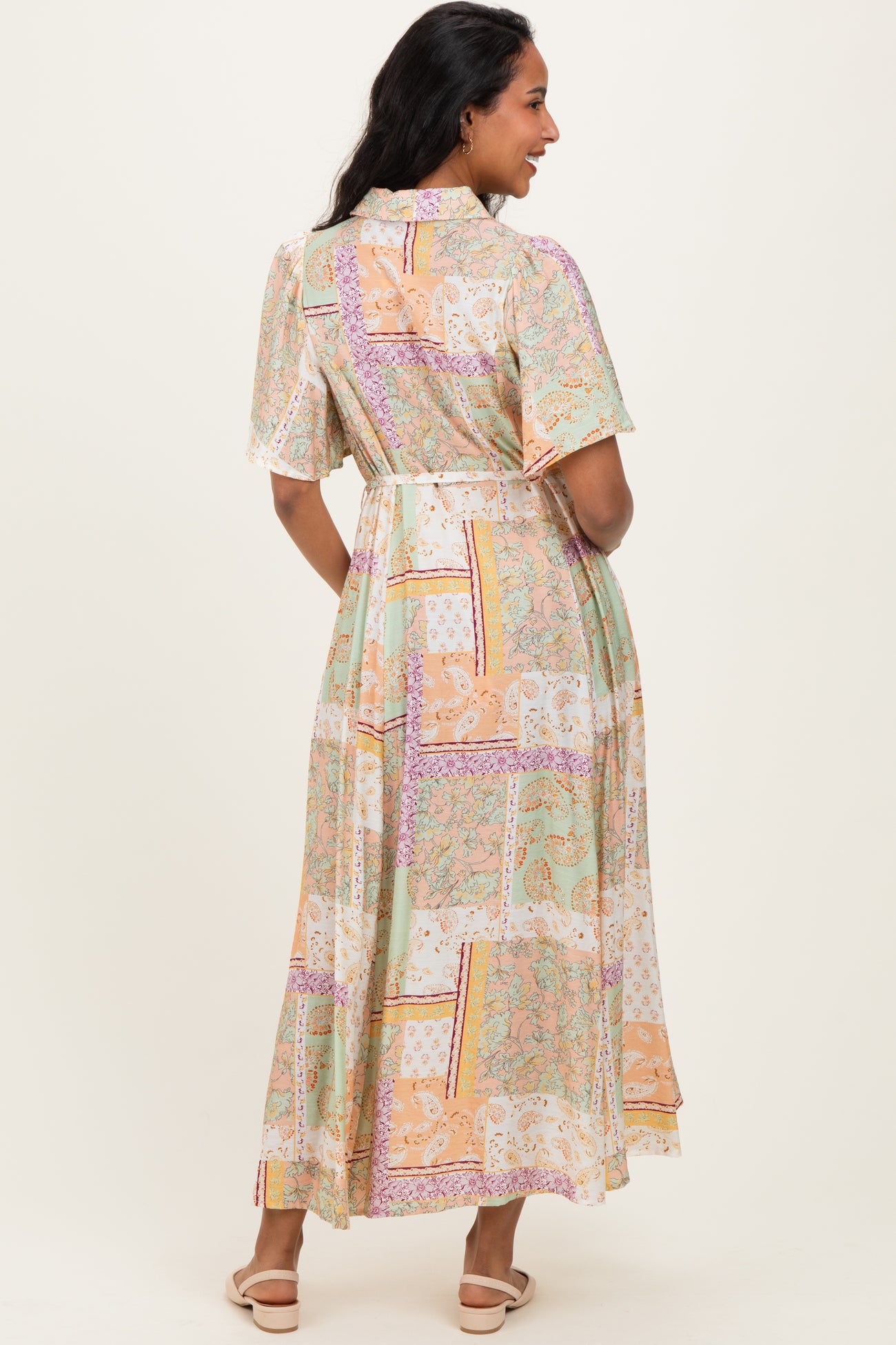 woman wearing a flowy pastel patterned maternity dress with short sleeves and a cinched waist, showing her baby bump