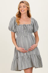 woman wearing a black and white gingham maternity dress with puff sleeves and a tiered skirt, holding her baby bump