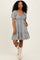 woman wearing a striped puff sleeve dress with a square neckline and ruffled hem, standing with one hand in the pocket