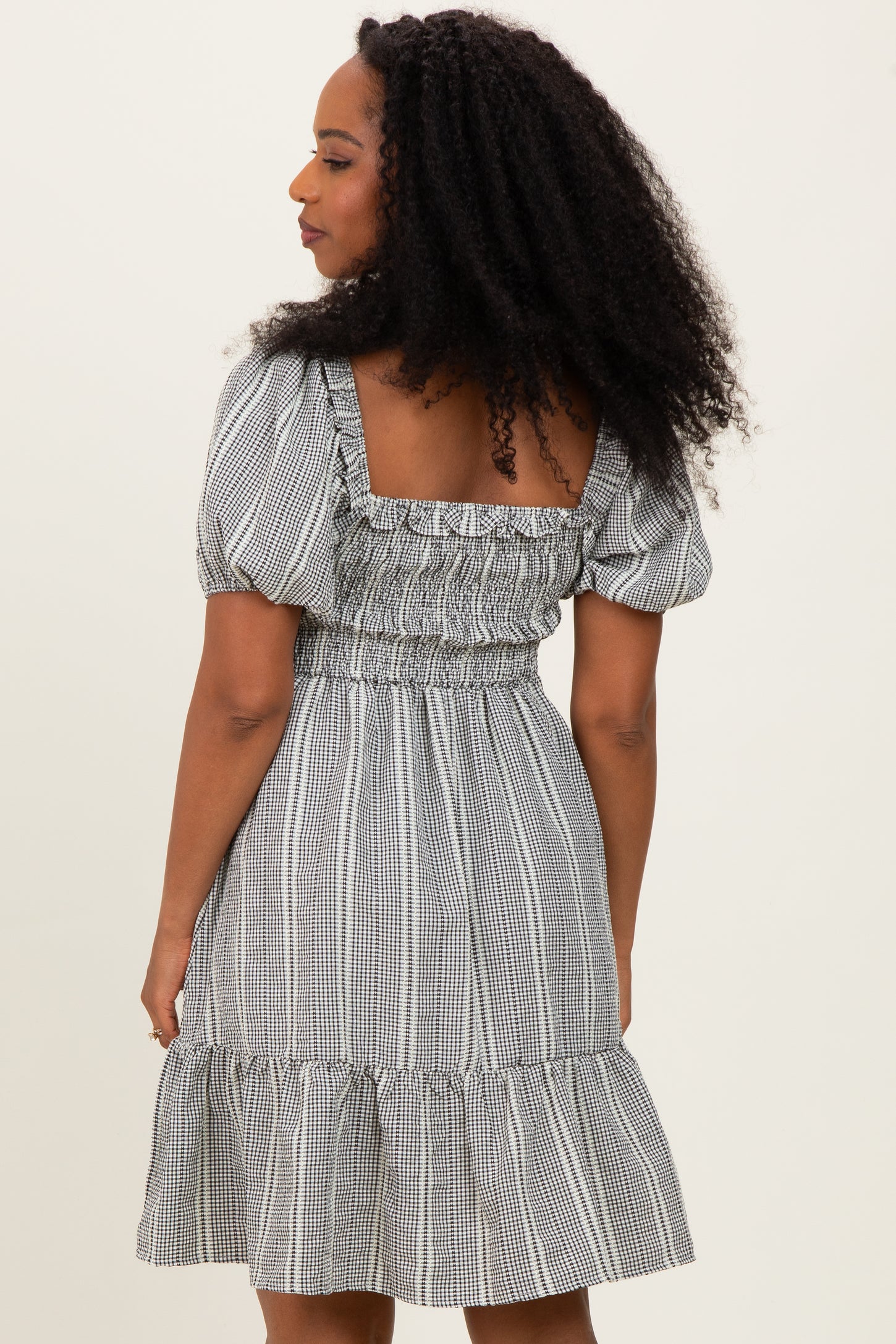 woman wearing a black and white checkered puff sleeve dress with a smocked bodice and ruffled hem