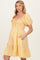 woman wearing a yellow gingham maternity dress with puff sleeves and a tiered skirt, featuring pockets