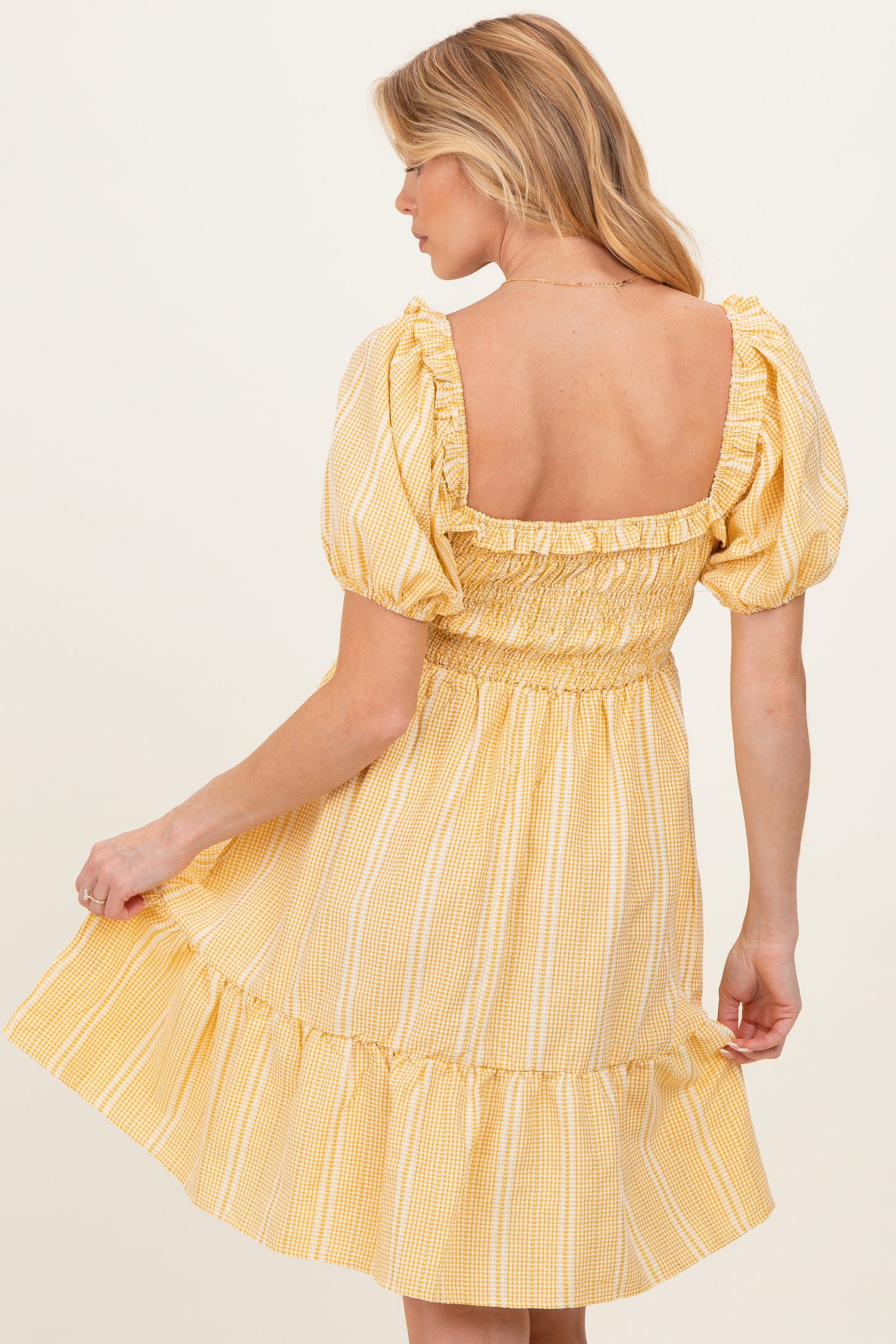 woman wearing a yellow striped maternity dress with puff sleeves and a smocked bodice, showing her back