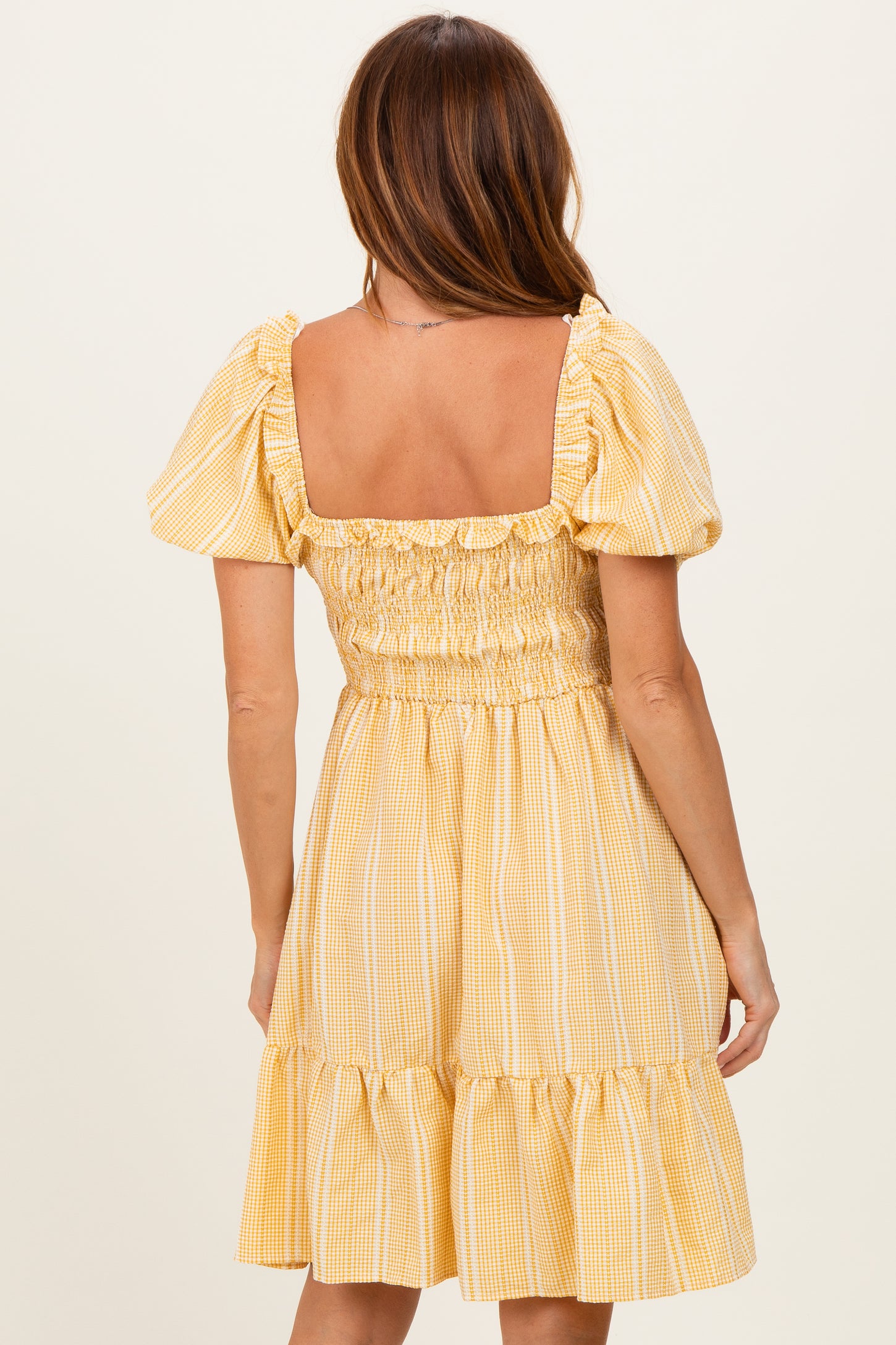 woman wearing a yellow checkered puff sleeve dress with a smocked bodice and a tiered skirt