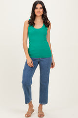 woman wearing a green ribbed tank top and blue straight-leg jeans, standing with a neutral background