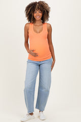 woman wearing an orange ribbed maternity tank top and light blue jeans, gently cradling her baby bump
