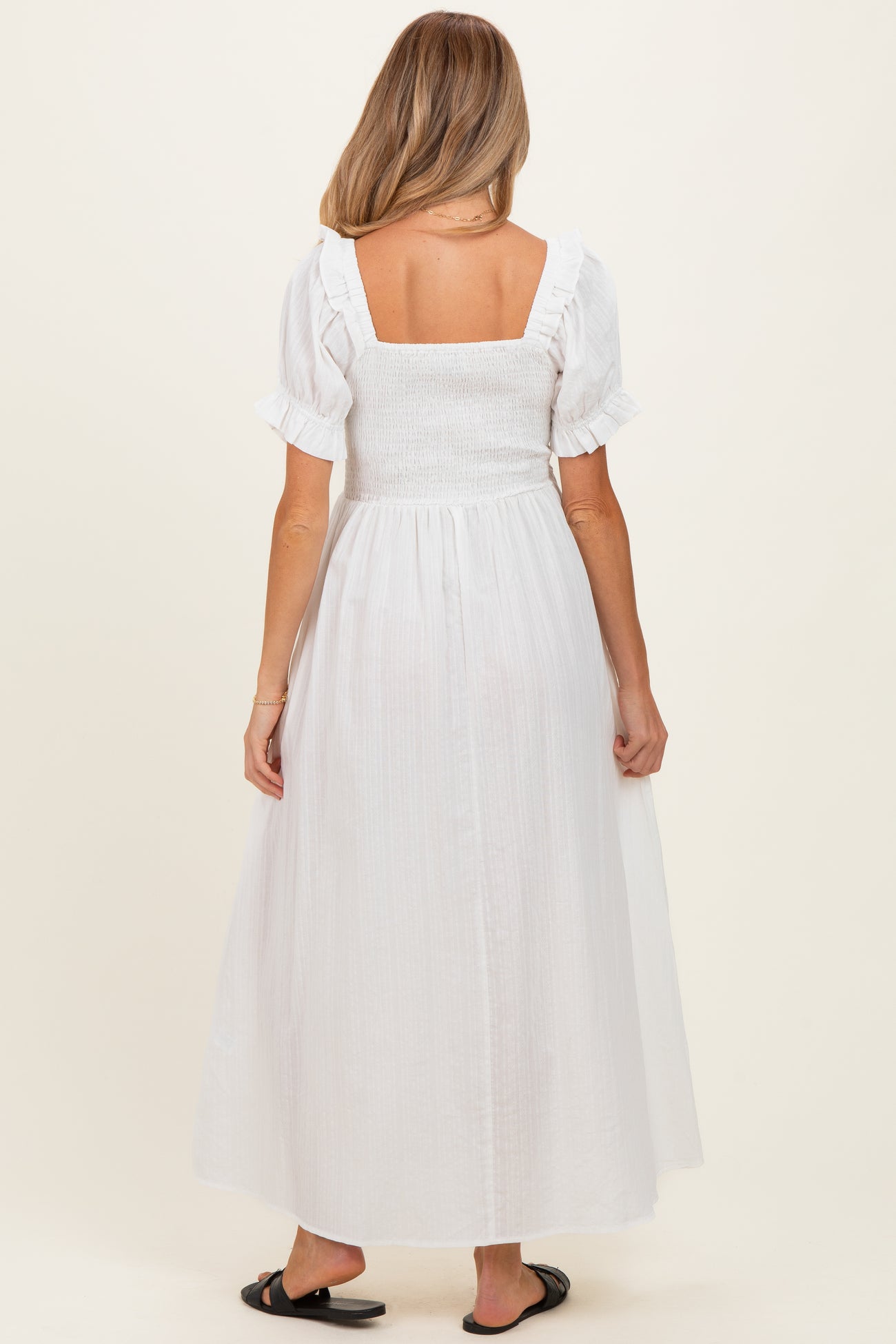 woman wearing a white maternity dress with a smocked bodice and ruffled sleeves, shown from the back