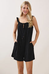 woman wearing a black striped romper with ruffle straps and buttons, featuring front pockets