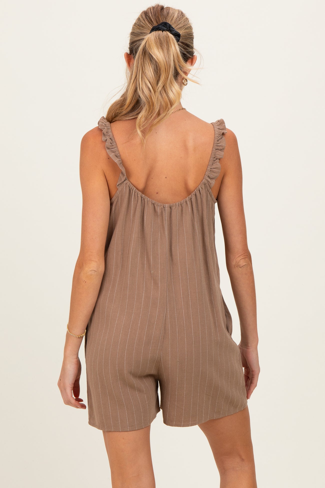woman wearing a brown striped maternity romper with ruffle details on the straps, showing her back