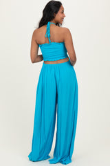 woman wearing a bright blue maternity crop top and wide-leg pants, showing a baby bump from the back