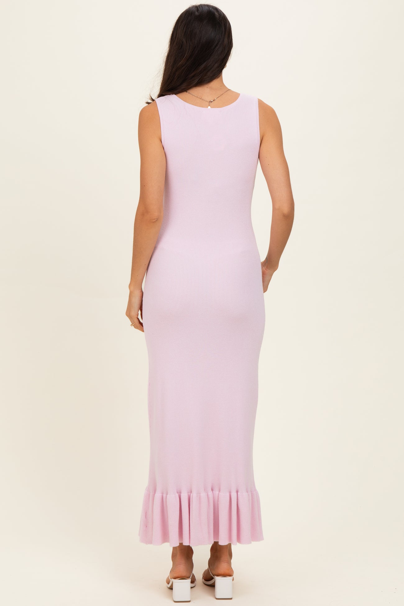 woman wearing a pale pink ribbed maxi dress with a ruffled hem, viewed from the back