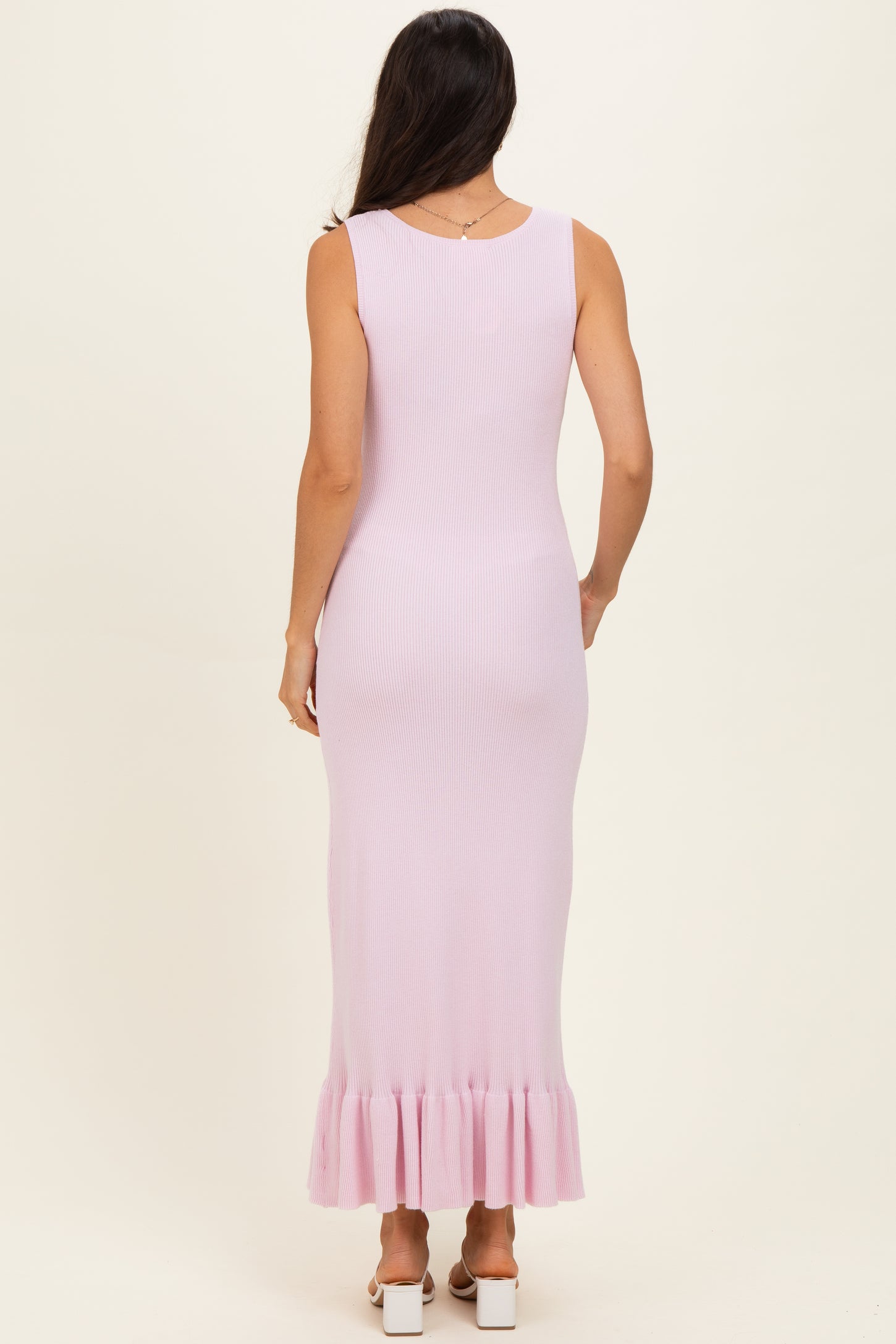 woman wearing a pale pink ribbed maxi dress with a ruffled hem, viewed from the back