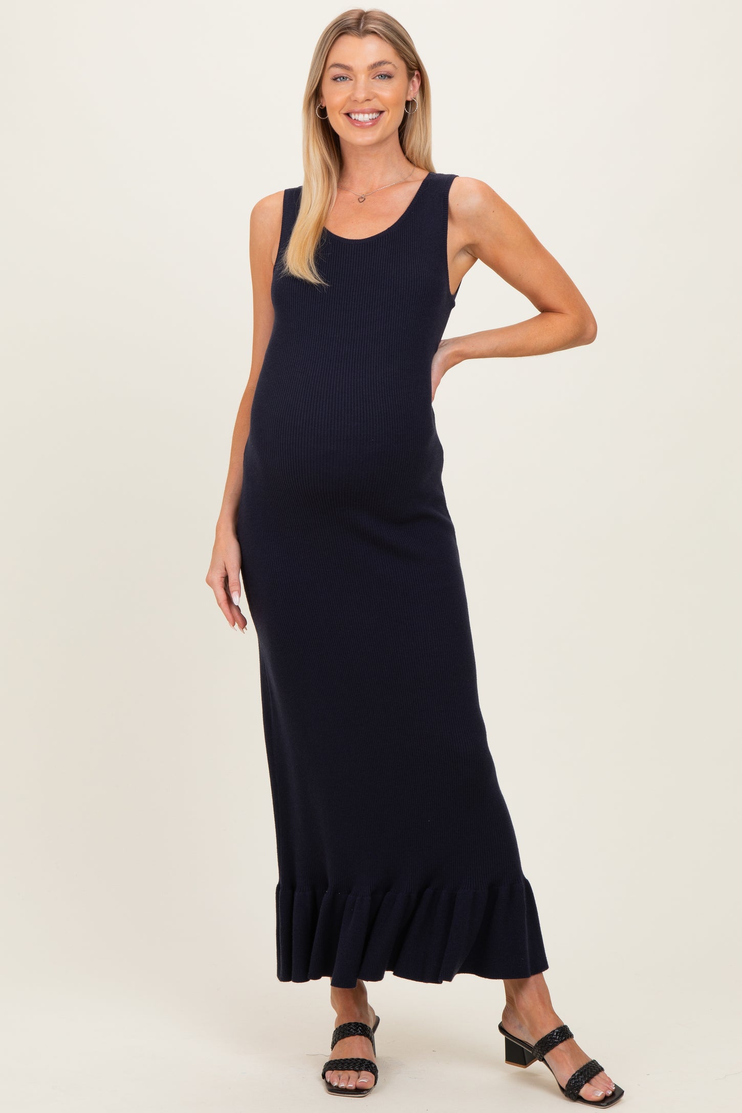 woman wearing a navy blue ribbed maternity maxi dress with a ruffled hem and a visible baby bump