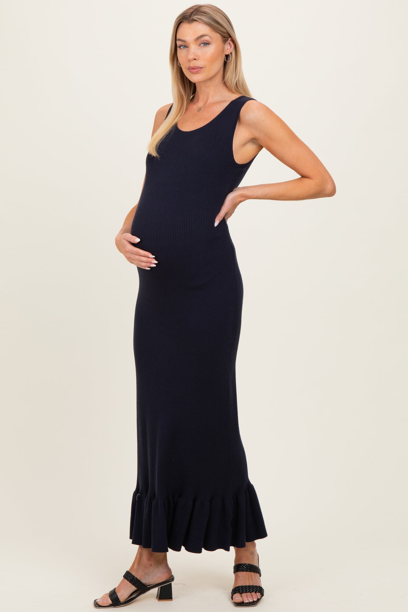 woman wearing a navy blue ribbed maternity dress with a ruffled hem and holding her baby bump