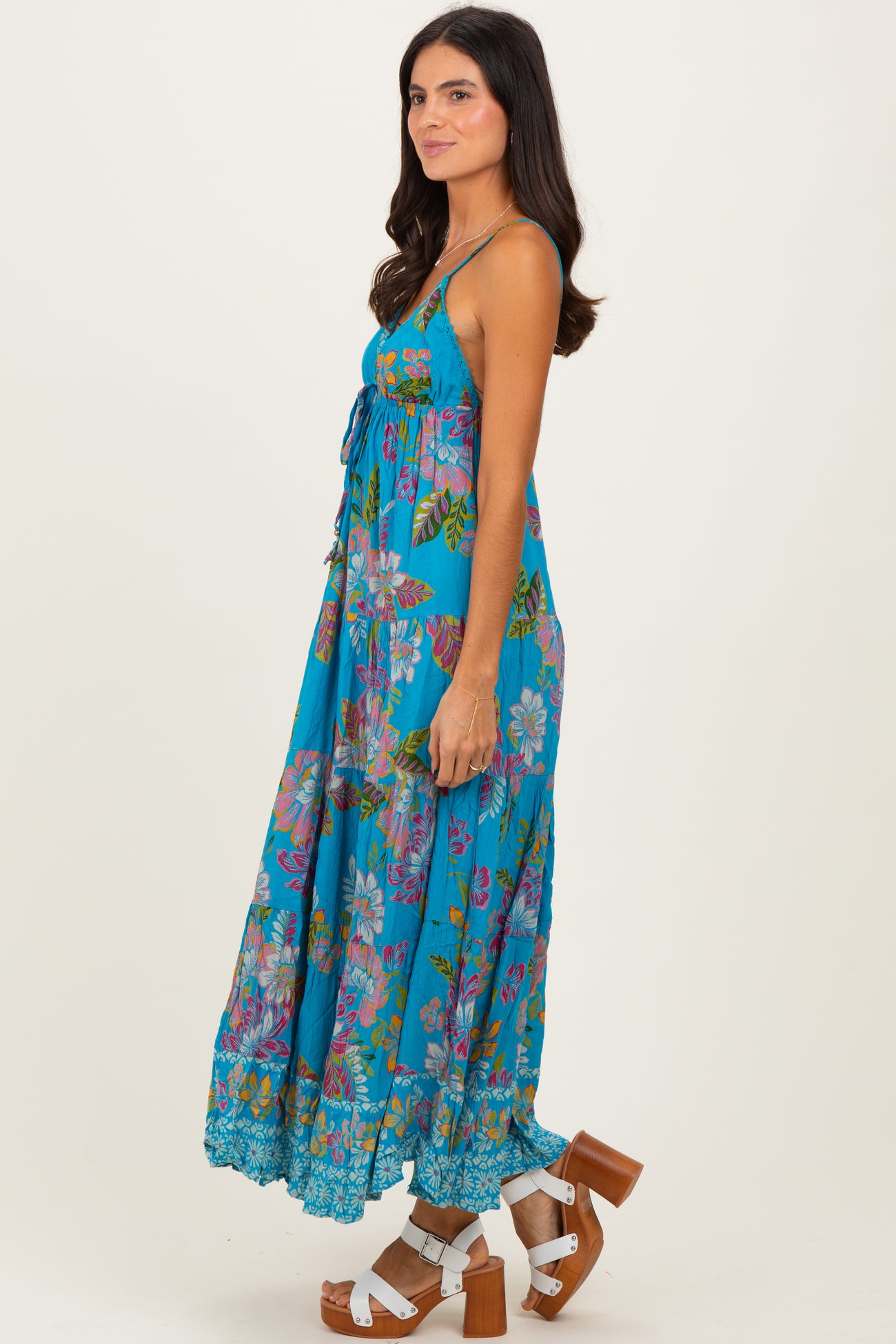 woman wearing a turquoise floral maxi dress with a tie front and tiered skirt, paired with brown block heel sandals