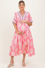 woman wearing a pink maternity dress with a leaf print and holding her baby bump