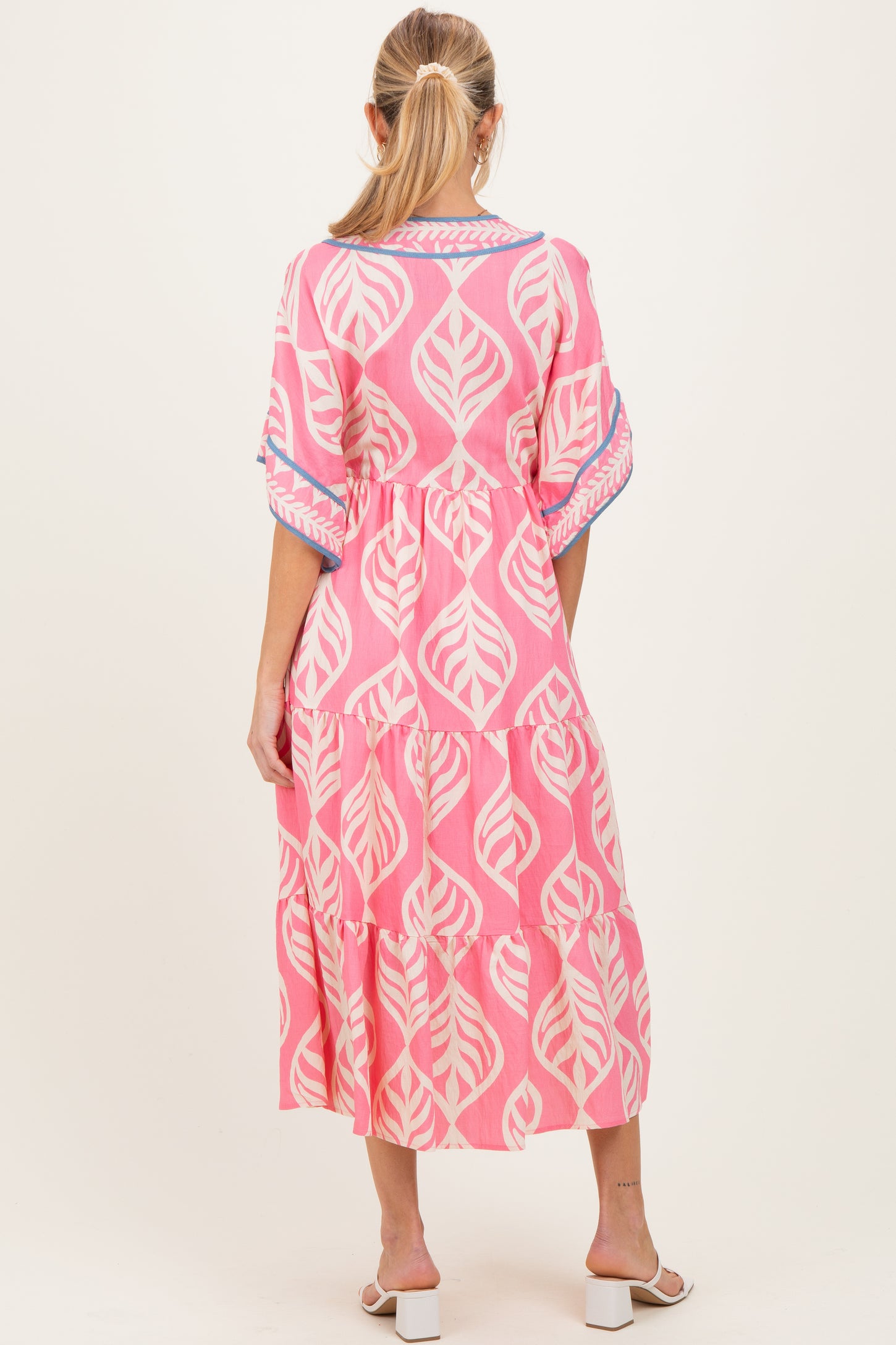 woman wearing a pink maternity dress with a leaf print and tiered skirt, seen from the back