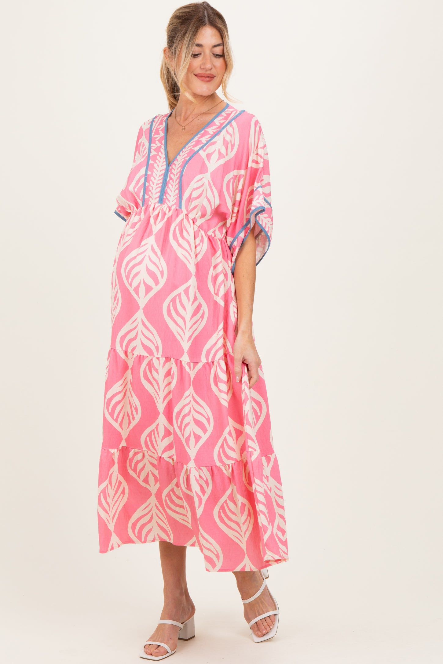 woman wearing a pink floral maternity maxi dress with tiered ruffles and a v-neckline, showing a baby bump