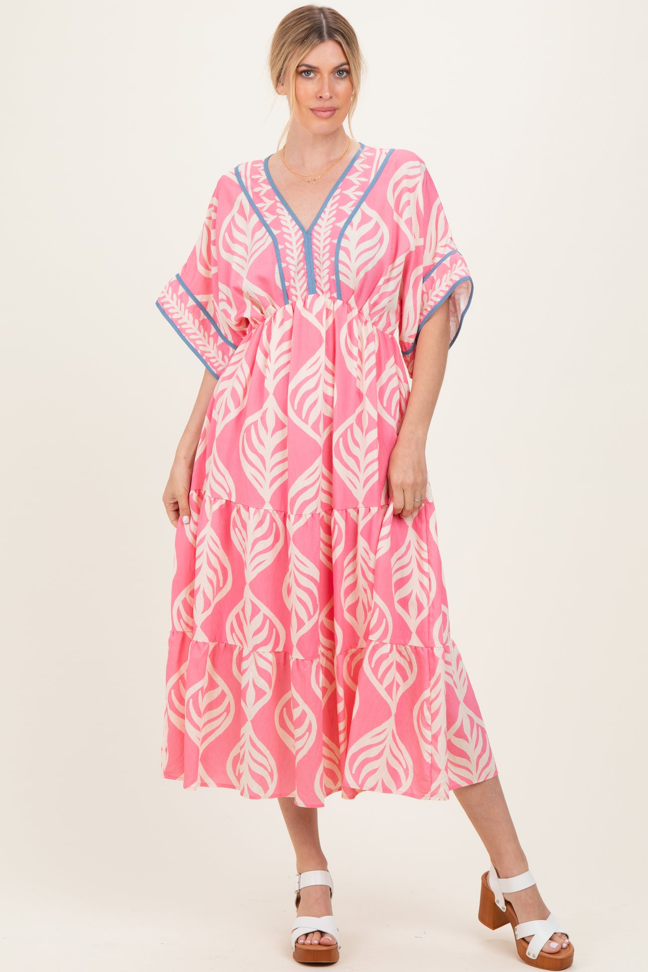 woman wearing a pink leaf print maxi dress with a v-neck and tiered ruffle hem, styled with white block heel sandals