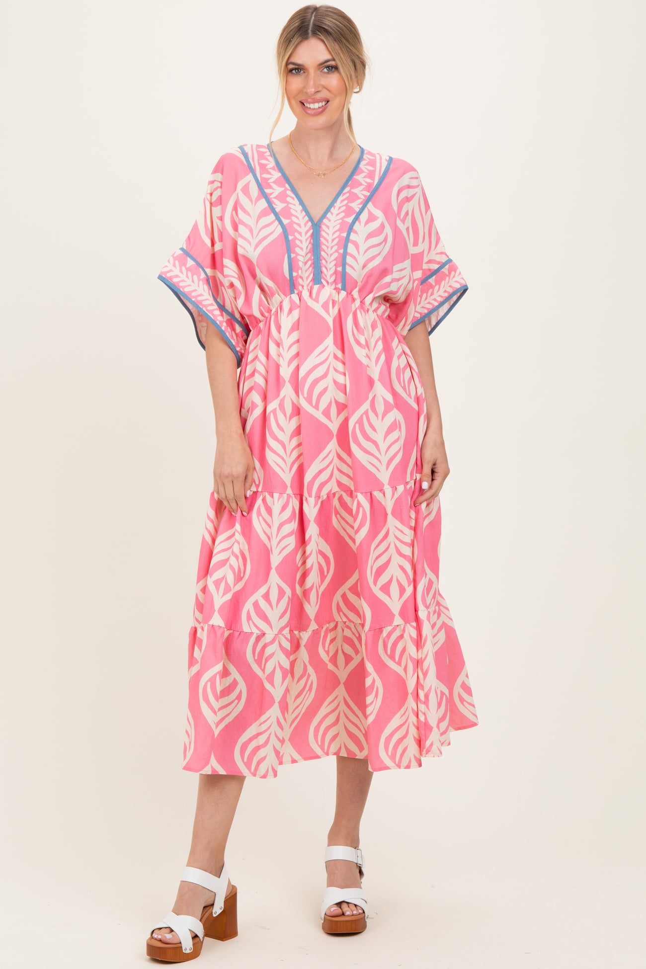 woman wearing a pink leaf patterned maxi dress with a v-neck and tiered skirt, styled with white block heel sandals