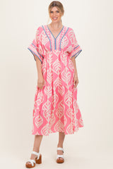 woman wearing a pink leaf patterned maxi dress with a v-neck and tiered skirt, styled with white block heel sandals