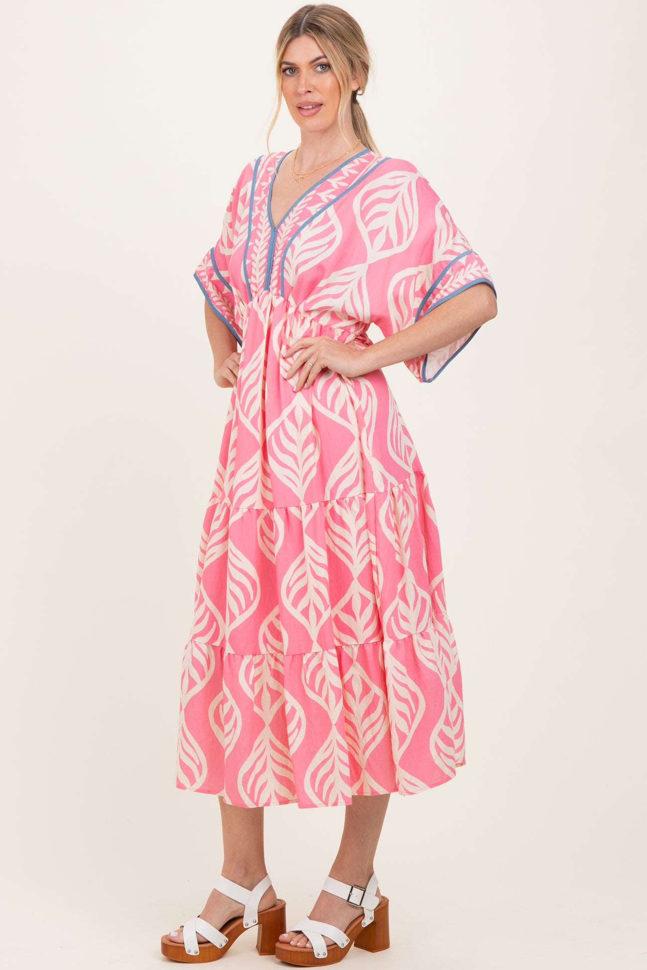woman wearing a pink boho style dress with leaf patterns and a tiered design, standing with one hand on her hip