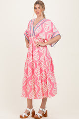 woman wearing a pink boho style dress with leaf patterns and a tiered design, standing with one hand on her hip
