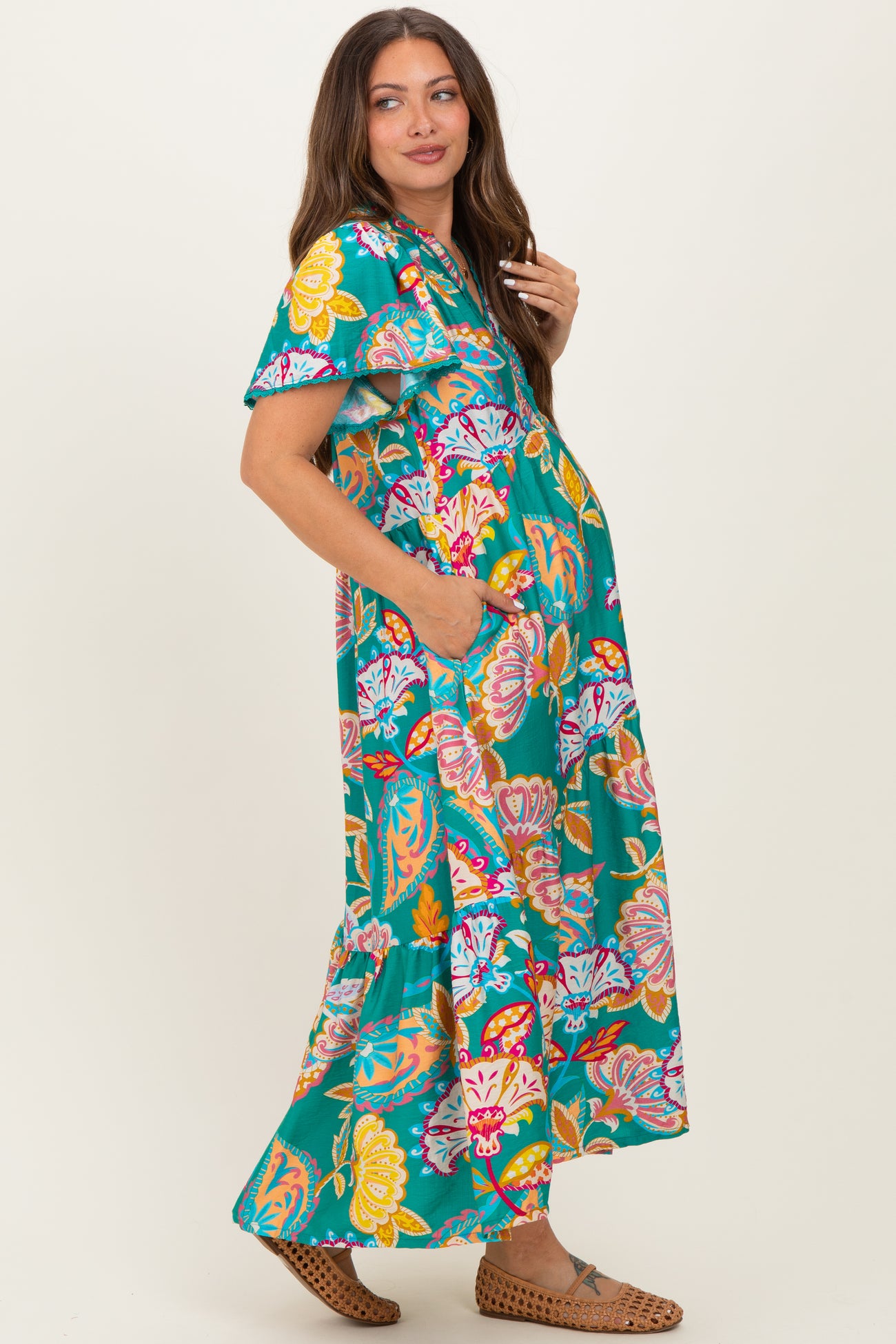 woman wearing a vibrant floral print maxi maternity dress with short sleeves and pockets, showcasing her baby bump