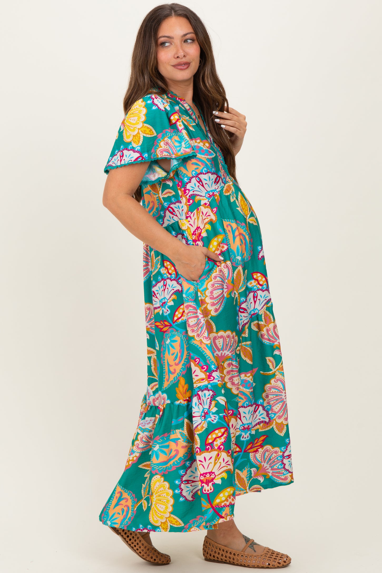woman wearing a vibrant floral print maxi maternity dress with short sleeves and pockets, showcasing her baby bump