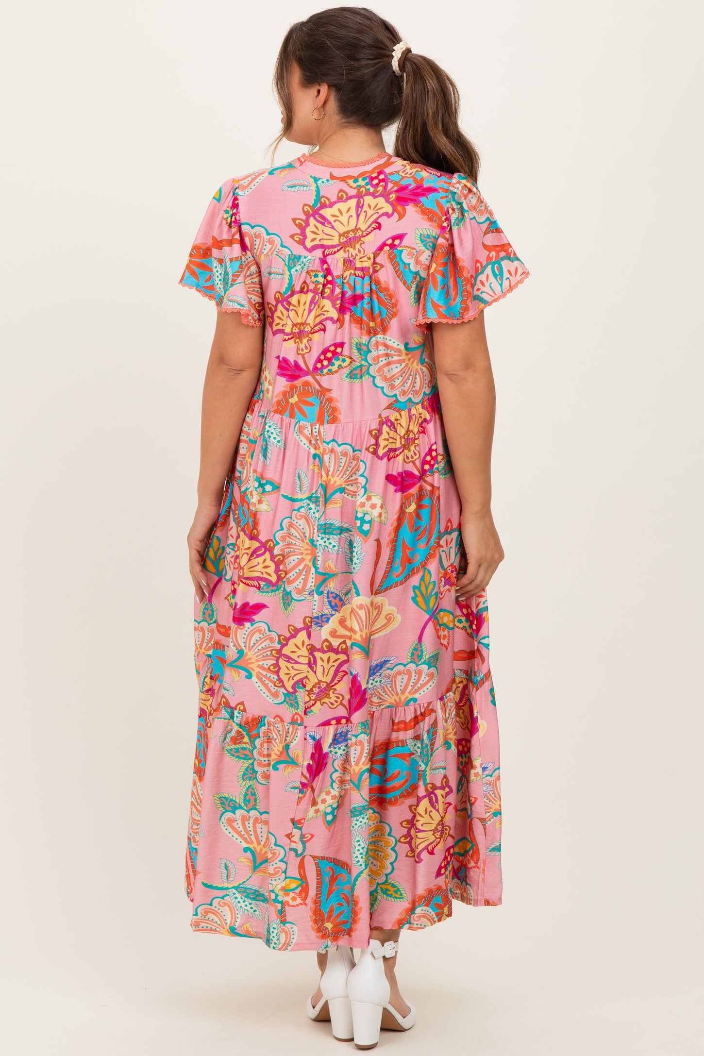 woman wearing a pink floral patterned maternity maxi dress with flutter sleeves and a tiered skirt