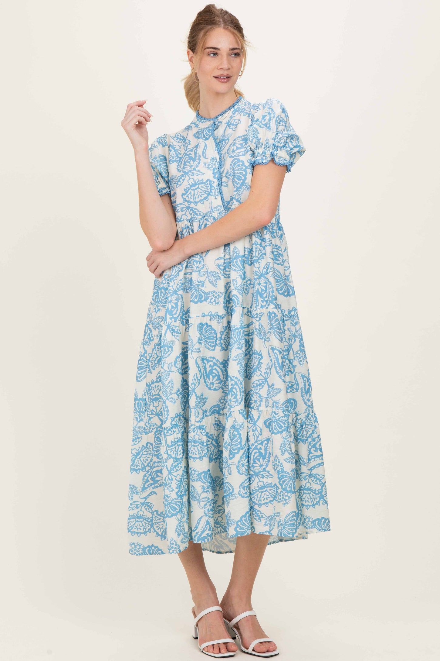 woman wearing a blue floral midi dress with puff sleeves and a high neckline, standing against a neutral background