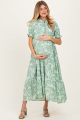 woman wearing a green floral print maternity dress and cradling her baby bump