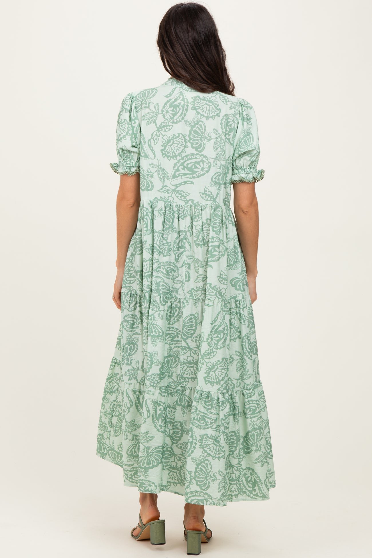woman wearing a green floral maxi dress with puff sleeves and a tiered skirt, shown from the back