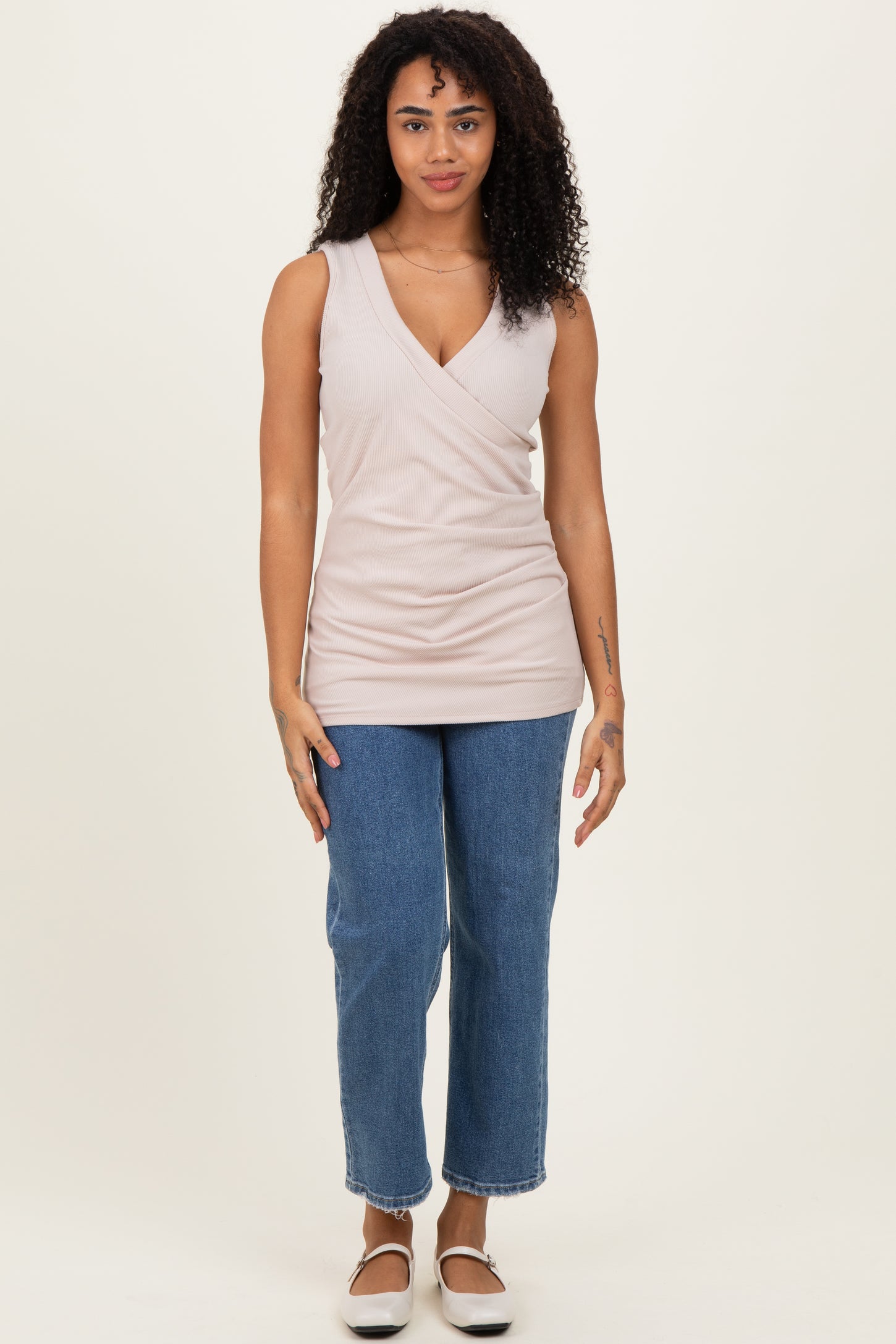 woman wearing a light pink sleeveless wrap top and high-waisted blue straight leg jeans