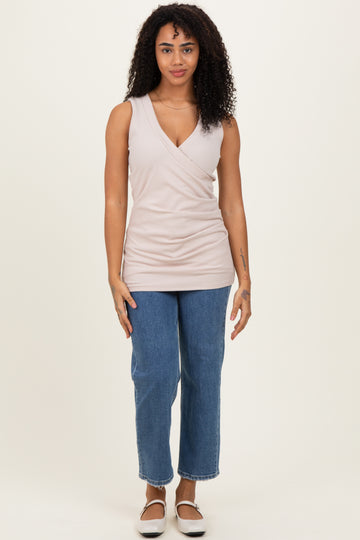 woman wearing a light pink sleeveless wrap top and high-waisted blue straight leg jeans