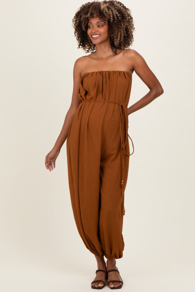 woman wearing a brown strapless maternity jumpsuit with a tie belt and relaxed fit, showing her baby bump