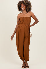 woman wearing a brown strapless maternity jumpsuit with a tie belt and relaxed fit, showing her baby bump