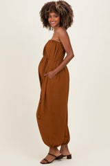 woman wearing a rust brown strapless maternity jumpsuit with pockets and a drawstring waist, showing her baby bump