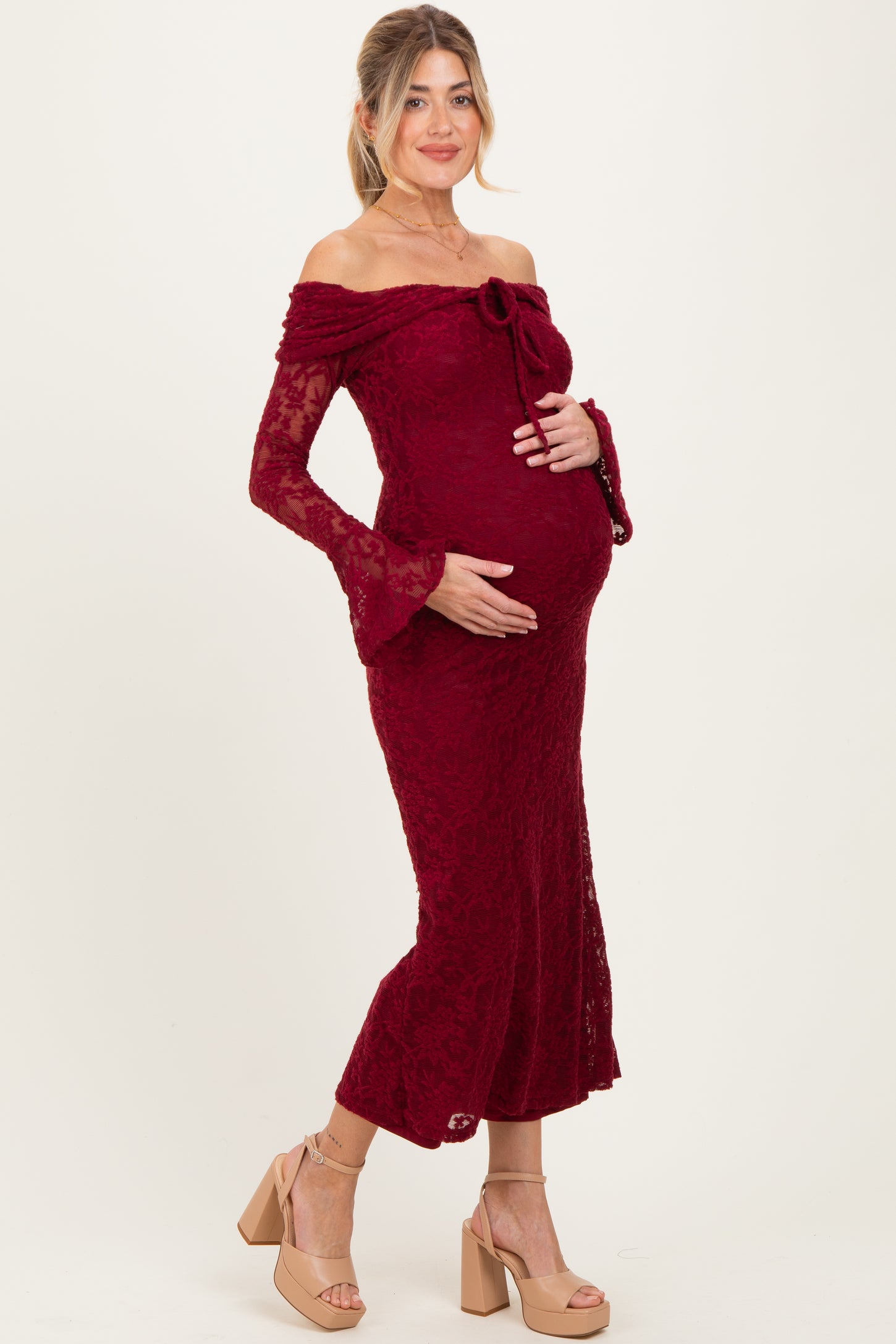 woman wearing a burgundy lace off-the-shoulder maternity gown and holding her baby bump