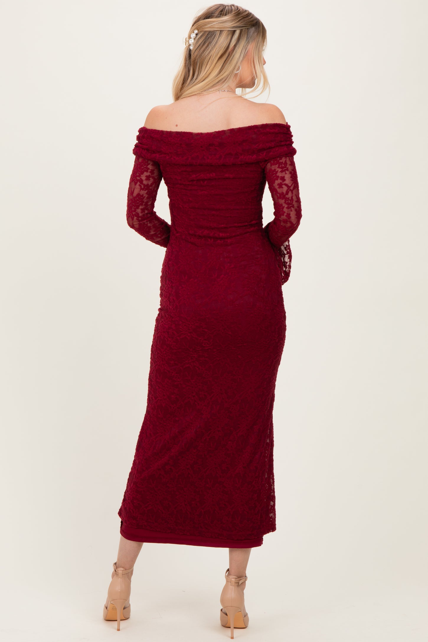 woman wearing a burgundy off-the-shoulder lace gown with long sleeves and a fitted silhouette, observed from the back